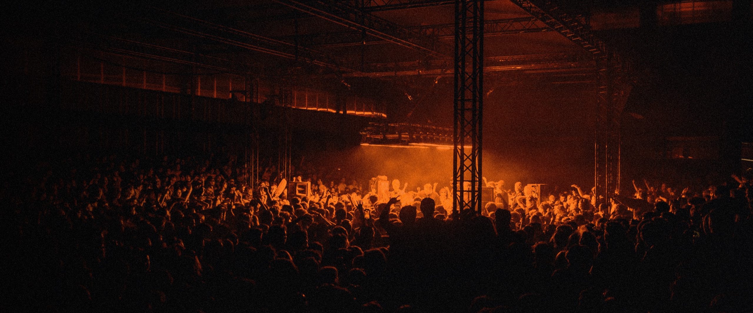 A packed warehouse night, graded in anyKrowd black and orange